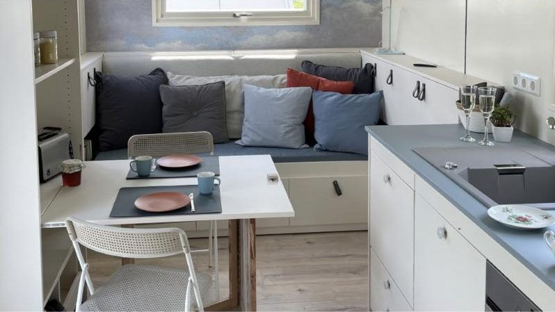 Essplatz mit Klapptisch, Sitzbank mit Kissen und Küchenzeile im Tiny House