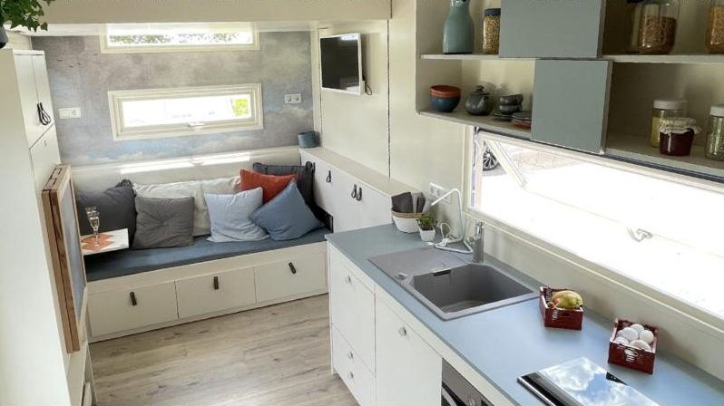 Küche mit Spüle und Kochfeld, dahinter Sitzbank mit Stauraum im Tiny House