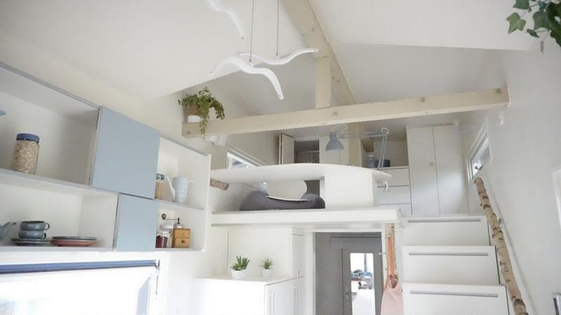 Helles Tiny House innen: Wohnbereich mit Regalen, Treppe und Schlafloft unter dem Dach