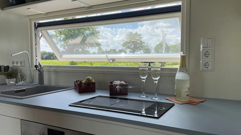 Küche im Tiny House mit nach außen aufklappendem Fenster und Blick auf die Wiese